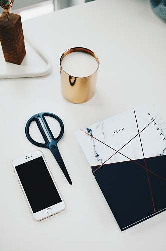 person silver iPhone 6 beside black scissors and white and black notepad on white table people