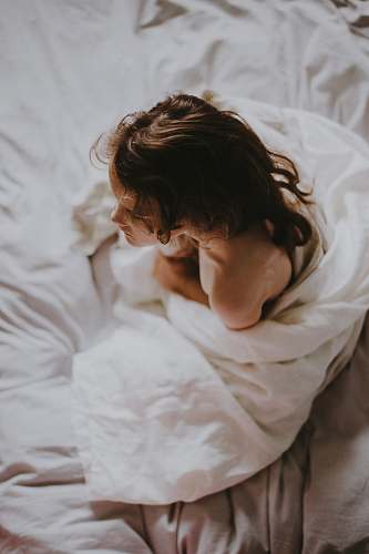 person woman sitting on bed covered with white blanket people