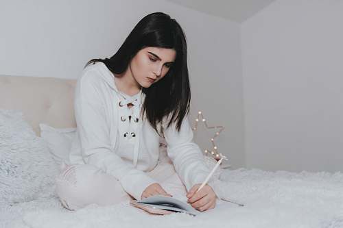 person woman sitting on bed while writing on notebook people