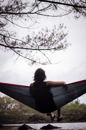 people woman sitting on hammock facing body of water person