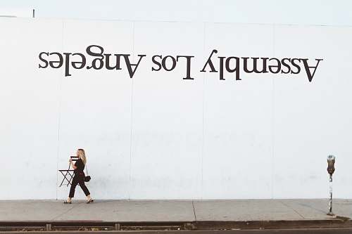 person woman walking beside white painted wall pedestrian