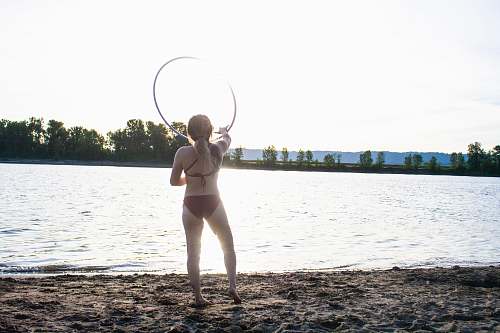 person woman wearing brown bikini holding hula hoop standing on seashore water