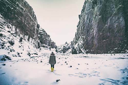 ice woman wearing gray coat standing in between mountain coated by snow nature