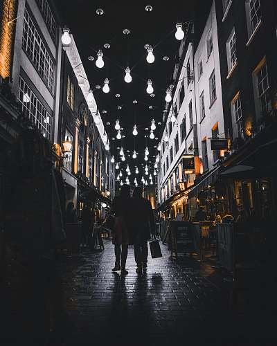 urban silhouette of couple walking under light bulbs between buildings city