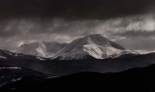 snow grayscale photography of mountain under cloudy sky mountain range