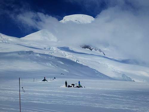 snow group of people standing on snow near tipi tent and snow covered mountain under white clouds during daytime glacier