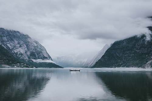 snow white and gray boat in the middle of calm body of water near mountain under white sky nature