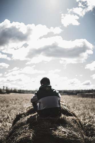 outdoors grayscale photography of man siting on hay grass field