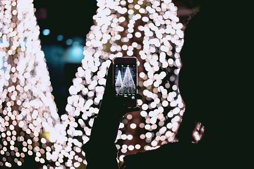 dark person taking picture of Christmas trees lights