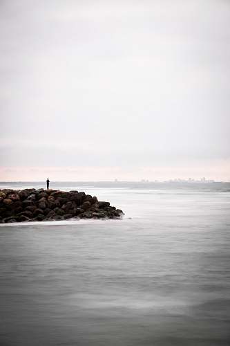 ocean person standing on rocks surrounded by body of water water