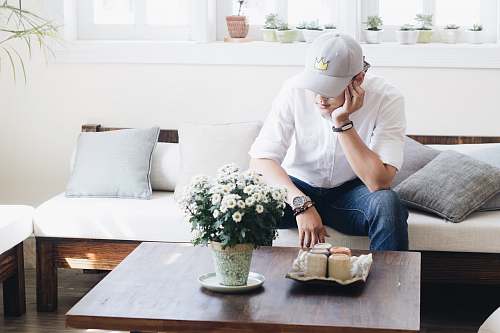 plant man sitting on white fabric sofa infront of coffee table inside the living room couch