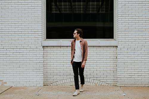 human man standing beside beige brick wall person