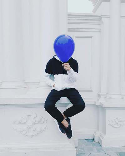 person person sitting on white concrete pavement holding blue balloon at daytime human