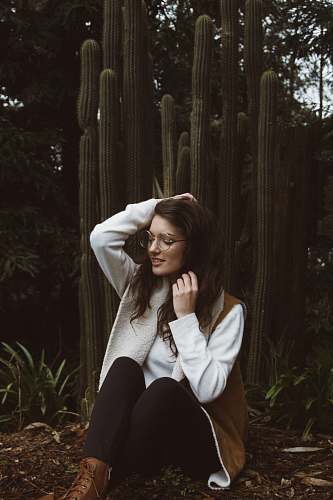 woman smiling woman wearing brown and white coat sitting beside green cacti plants human