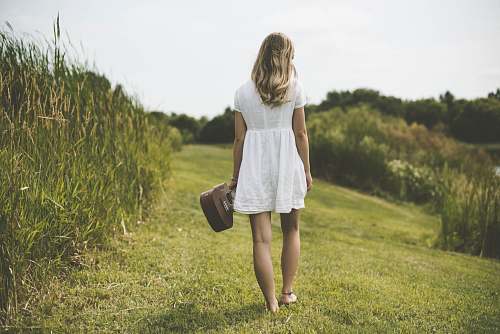 person woman holding ukulele while walking on grass field surrounded with tall grasses human