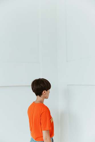 human woman wearing orange shirt facing white wall person