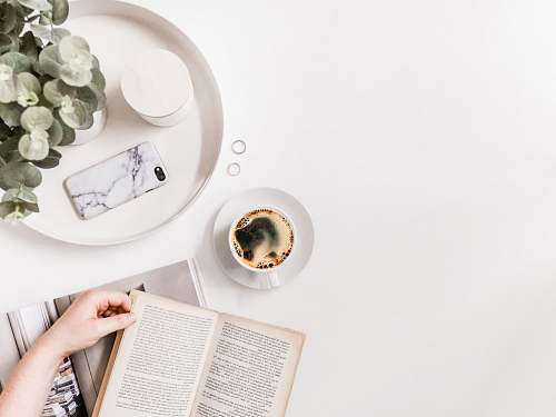 page flat-lay photography of person holding opened book on tabletop beside cup of black coffee text