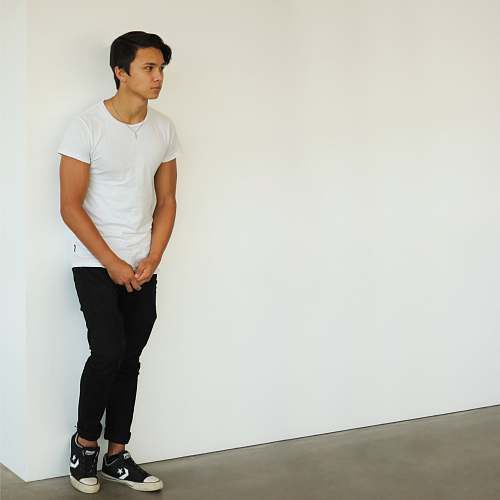 human man wearing white t-shirt and black jeans standing near white wall apparel
