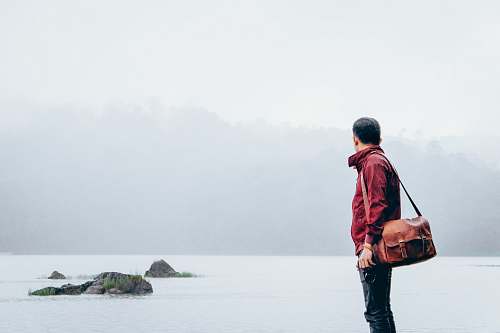human man with messenger bag looking towards the sea people
