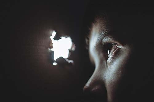dark person watching through hole light