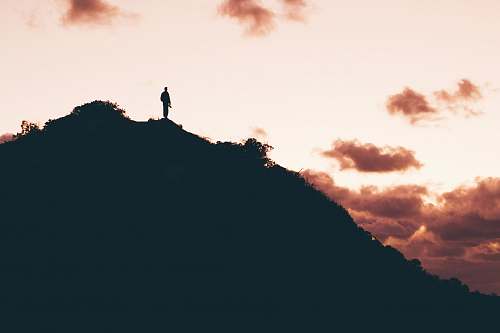 sunset photo of man standing on top of mountain black