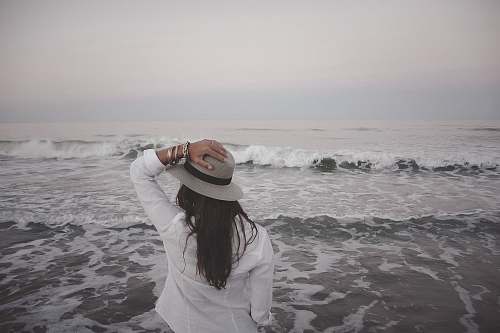 people woman holding hat beside body of water beach