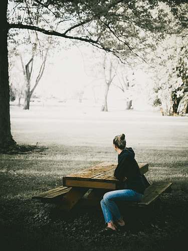 human woman in black hoodie and blue denim jeans sitting on picnic bench sitting