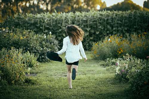 human woman running on grass surrounded with flowers during daytime people