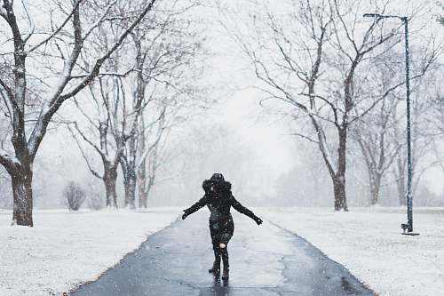 people woman wearing black parka jacket standing on road near tall trees and light post during daytime human