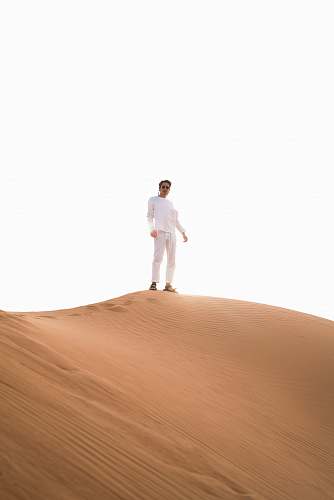white man standing atop desert sand dune desert