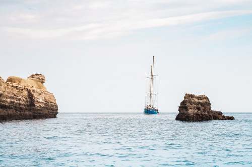 rock blue boat between brown rock formation under blue and white sky at daytime ocean