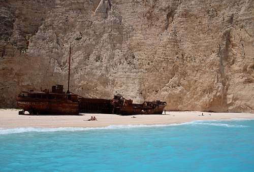 shipwreck group of people on seashore near ship near mountain at daytime greece