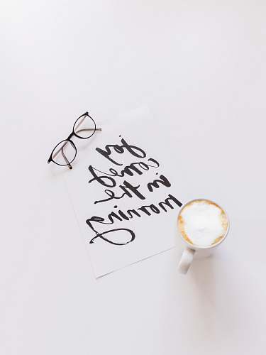 handwriting black framed eyeglasses beside white ceramic coffee cup calligraphy
