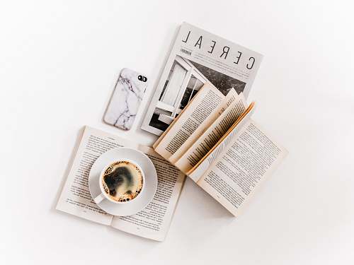 page white ceramic cup with coffee on saucer beside opened books white