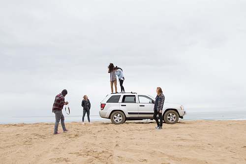 car two people standing on Jeep Grand Cherokee SUV while the other person camera on sand during daytime transportation