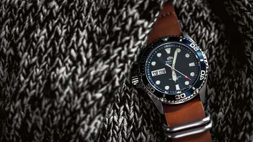 wristwatch round black analog watch with brown leather strap on black and white knitted textile texture