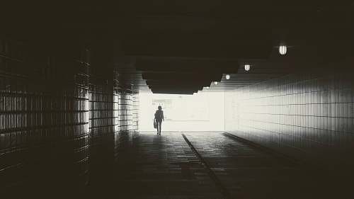 corridor gray scale photography of person walking in bridge light