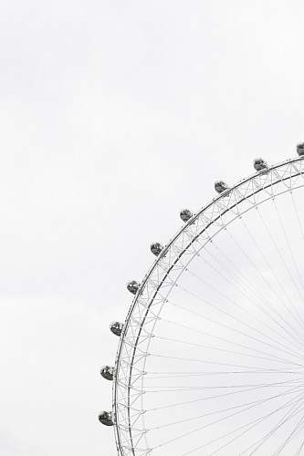 black-and-white Part of a ferris wheel with enclosed cars for riding in and people in the cars against an overcast sky minimal
