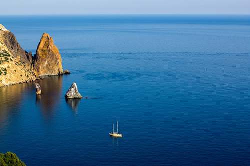 sea aerial photography of white ship on sea near rock formations under blue sky during daytime water