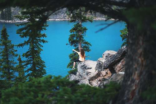 tree girl sitting on cliff near trees pointing towards body of water landscape