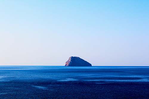 sea islet on body of water under cumulus clouds ocean