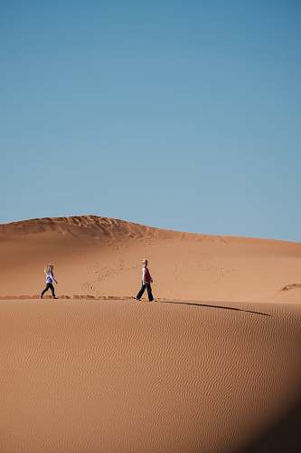 desert man and woman walking on brown sands dune