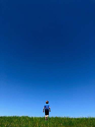 person man in blue t-shirt and black shorts walking in green grass field human