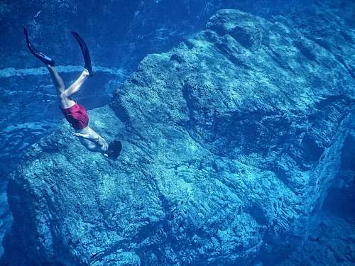 water man in red shorts swimming near huge underwater rock diver