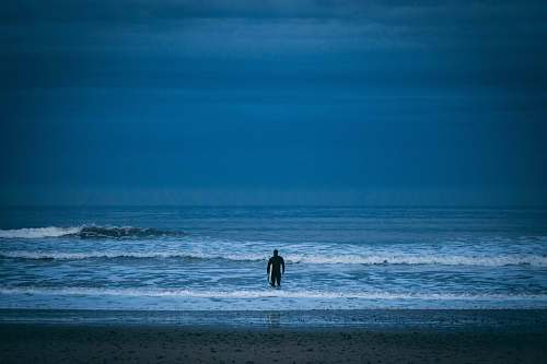 ocean man standing on beach under cloudy sky sea