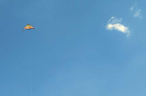 gliding orange and green kite in the sky soaring at daytime leisure activities