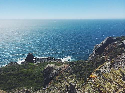 cliff person sitting on cliff near body of water coast