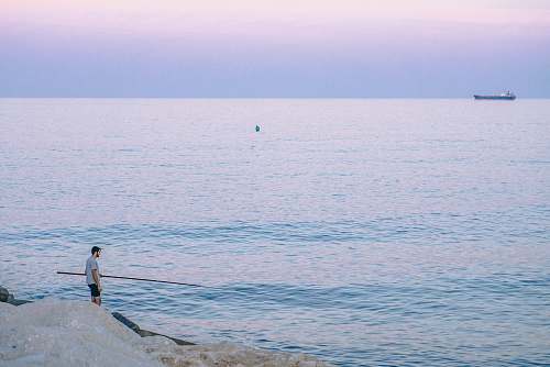 sea person standing on rock holding stick facing body of water during golden hour man