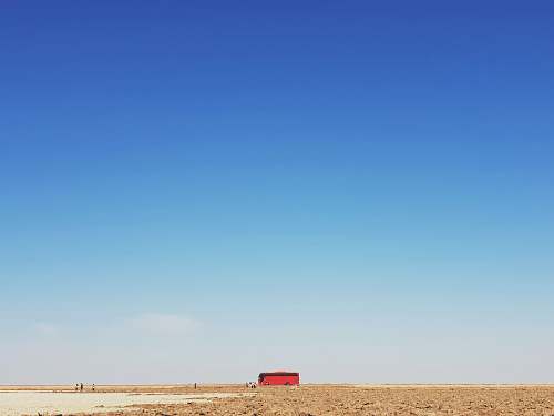 outdoors red bus traveling on brown desert plain nature