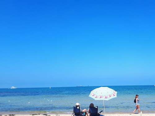 human two women sitting by the seashore during daytime person